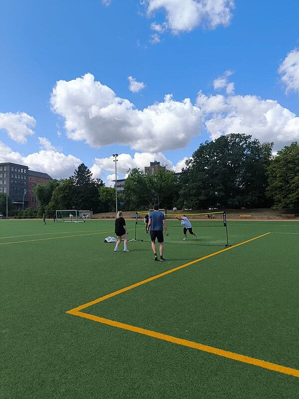 Schnitzeljagd, Tombola und Volleyball-Turnier Einige Teilnehmende des Sommerfestes der Euro Akademie Berlin spielen auf dem großen Fußballplatz, auf dem sie ein Netzaufgebaut haben, Volleyball.