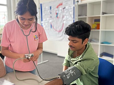 Eine junge Frau misst mit einem Blutdruckgerät den Blutdruck eines jungen Mannes.