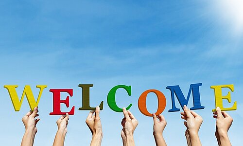 Hände halten bunte Buchstaben hoch, die das Wort Welcome bilden.