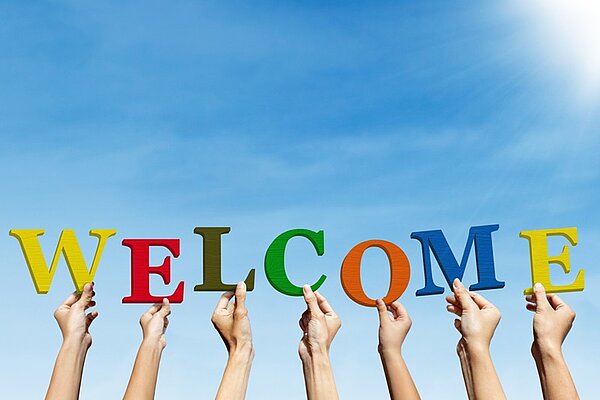 Hände halten bunte Buchstaben hoch, die das Wort Welcome bilden.