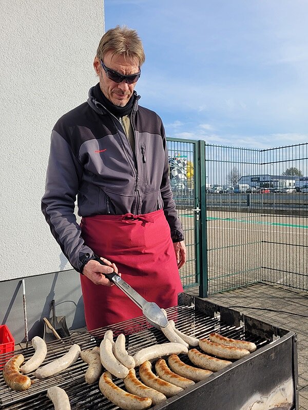 Mitarbeitender steht am Außengrill und grillt Würstchen.