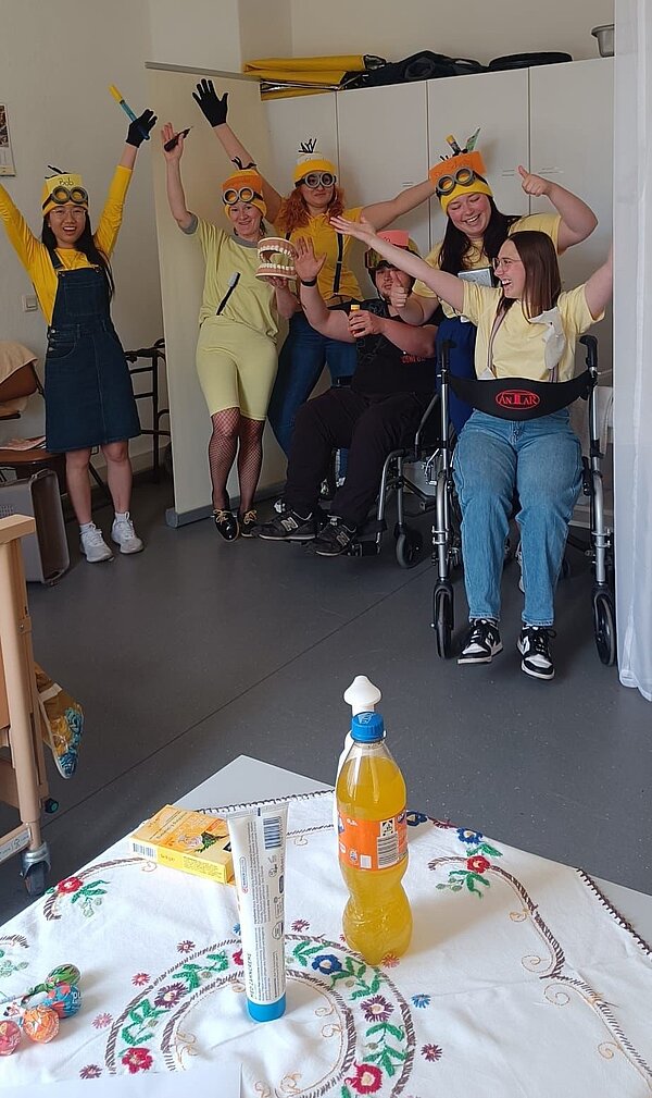 Operation Krankmacher: Die Mission der Minions Fröhliches Gruppenbild von Schülerinnen und Schülern im Minionkostüm und Pflegeutensilien. Sie strecken die Arme hoch und lachen dabei.