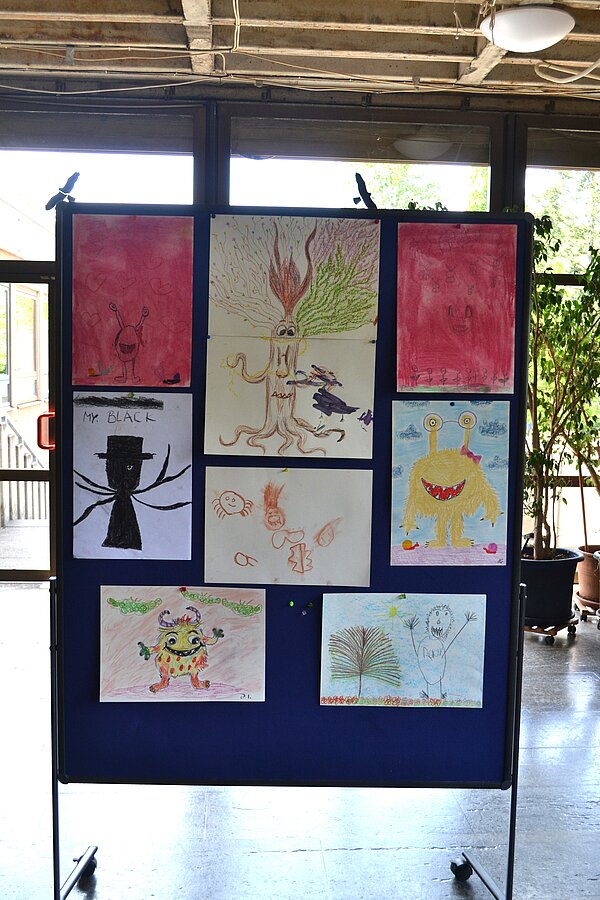 Vernissage in der Christopherus-Schule Eine Stellwand mit bunt bemalten Bildern steht in einem hellen Raum mit großen Fenstern.
