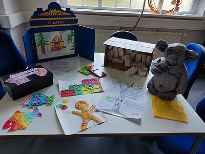 Auf einem großen Tisch liegen selbst gestaltete und gebastelte Bilder, Weihnachtskarten, ein kleines Puppentheater und eine Figur.