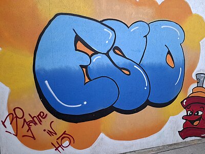 Auf einer Wand ist vor einem orangenen Hintergrund ein blaues Graffiti mit den Buchstaben ESO zu sehen.