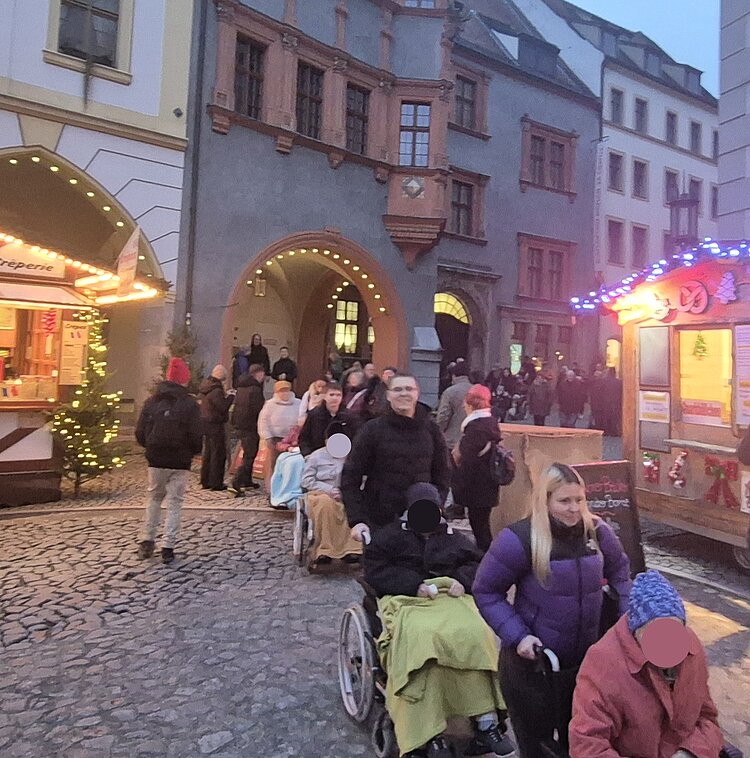 Pflegeheimbewohnende werden von angehenden Krankenpflegehelferinnen und -helfern über den weihnachtlich beleuchteten Weihnachtsmarkt in der Görlitzer Altstadt begleitet.