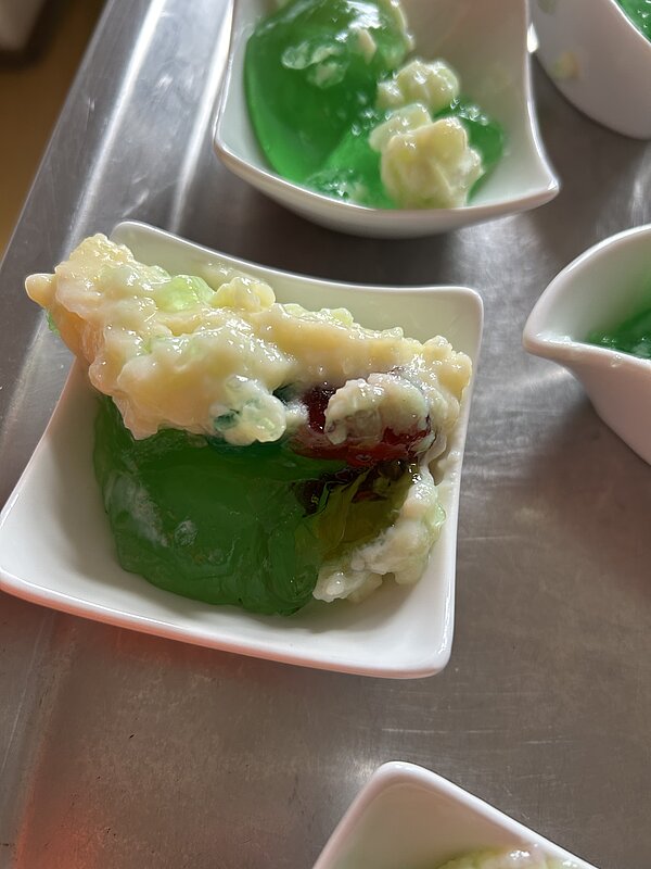 Kleine weiße Schälchen mit grünem Wackelpudding und heller Creme auf einem Metalltablett – Halloween-Dessert.