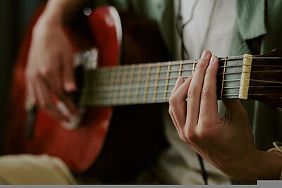 Kaukasischer Jugendlicher spielt zu Hause Akustikgitarre, Nahaufnahme von Händen, Streichern auf Griffbrett, Musikaufnahmen oder kreative Freizeitaktivitäten.