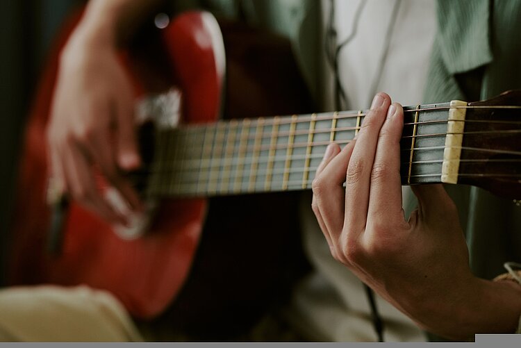 Kaukasischer Jugendlicher spielt zu Hause Akustikgitarre, Nahaufnahme von Händen, Streichern auf Griffbrett, Musikaufnahmen oder kreative Freizeitaktivitäten.