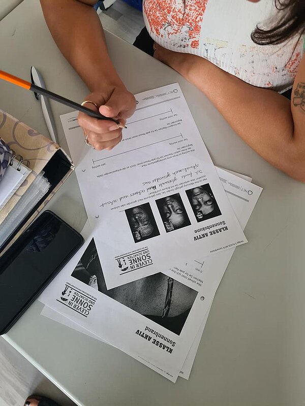 Auszeichnung „Clever in Sonne und Schatten“ 2024 Eine Schülerin sitzt über ein Handout gebeugt, Blick von oben auf ihren Tisch, auf dem neben den Handouts auch noch ein Ordner liegt.