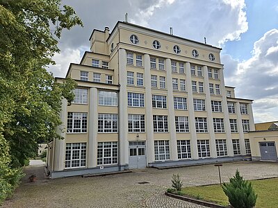 Außenansicht eines beigen und hellgelben Gebäudes mit vielen Fenstern.