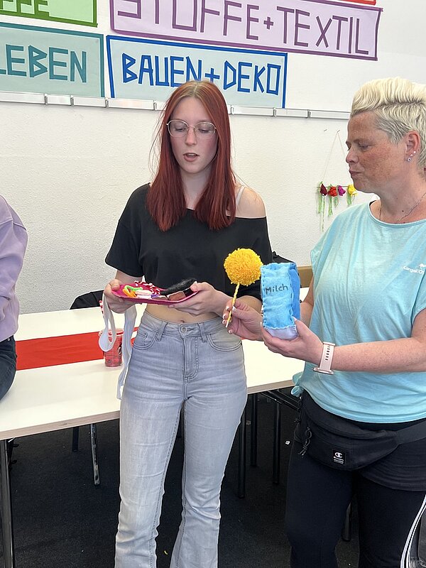Zwei Auszubildende zeigen stolz ihre kreativen Bastelarbeiten bei einem Workshop für Stoffe und Textilien.