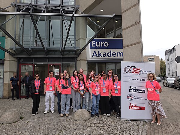 Gruppe von Teilnehmenden in pinken T-Shirts vor dem Gebäude der Euro Akademie neben einem Banner der ESO Education Group.