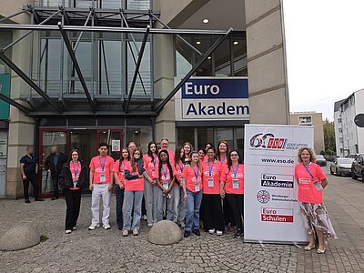 Gruppe von Teilnehmenden in pinken T-Shirts vor dem Gebäude der Euro Akademie neben einem Banner der ESO Education Group.
