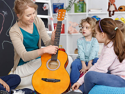 Eine Frau spielt Gitarre für Kinder in einer farbenfrohen, verspielten Umgebung.