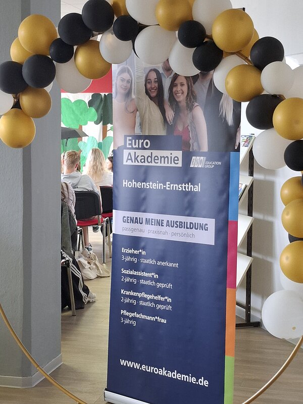 Roll-up der Euro Akademie Hohenstein-Ernstthal mit Informationen zu Ausbildungsangeboten, eingerahmt von einem Bogen aus schwarzen, weißen und goldenen Luftballons.