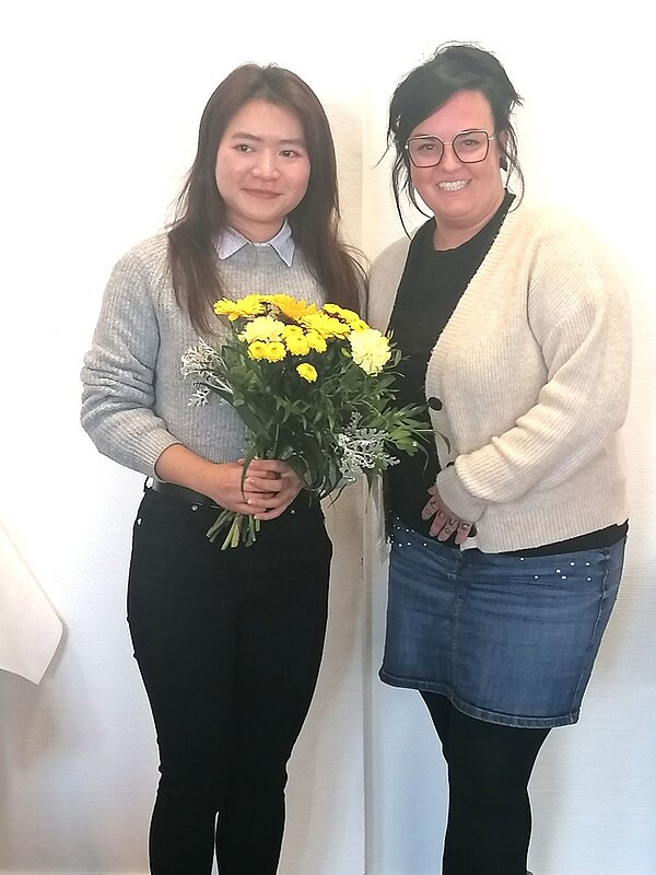 Eine Absolventin der Ausbildung zur Pflegefachfrau an der Euro Akademie Bitterfeld-Wolfen steht lächelnd neben einer Praxisanleiterin, die ihr einen bunten Blumenstrauß überreicht. Das Foto entstand bei der feierlichen Zeugnisübergabe.