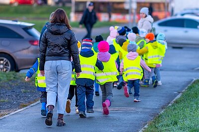 Eine Gruppe von Kleinkindern in gelben reflektierenden Westen, gehen mit ihren Erzieherinnen und Erziehern einen Spaziergang machen, um die Straßenverkehrsregeln zu lernen.