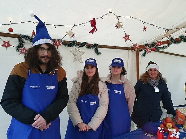 Euro Akademie Berlin begeistert beim Wintermarkt Schülerinnen und Schüler in blauen Euro Akademie Weihnachtsmützen und Schürzen am Wintermarkt-Stand.