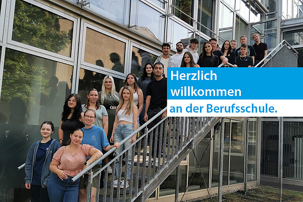 Ein Gruppe junger Leute steht auf eine Metaltreppe am Außenbereich einer Glasfassade eines Gebäudes und schau in die Kamera.