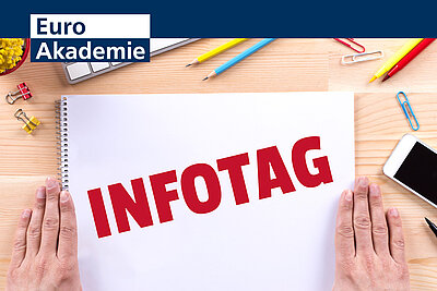 Auf einem weißen Blatt Papier steht in roter Schrift Infotag, das Blatt liegt auf einem Holztisch.