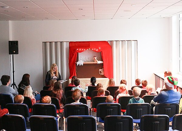 Kinder sitzen gespannt auf ihren Stühlen beim Puppentheater. 