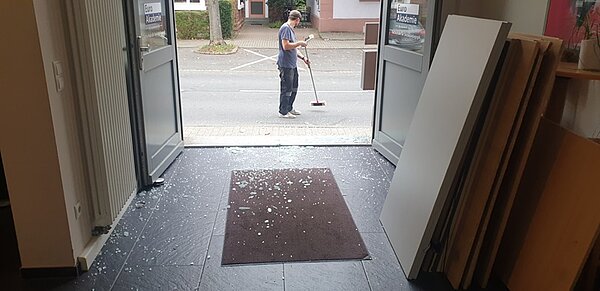 Mitarbeiter fegt die Scherben vor dem Haus zusammen.