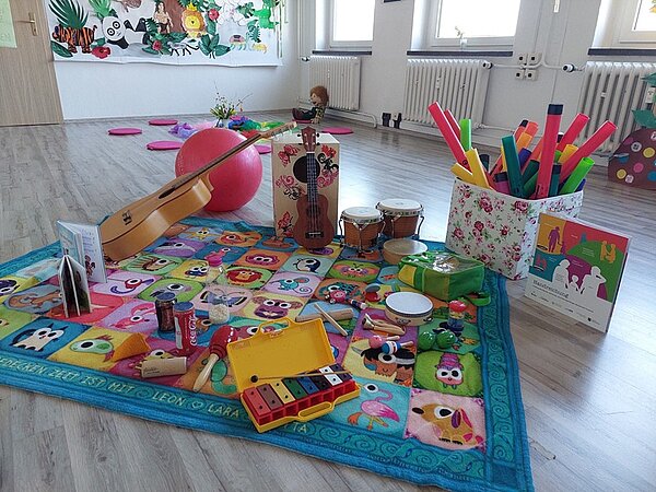 Es liegen allerlei bunter Kinderinstrumente auf einem ebenso bunten Teppich. 