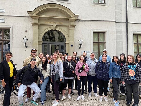 Die rund 25 weiblichen und männlichen Auszubildenden zu Pflegefachkräften an der Euro Akademie Jena  stehen vor dem Eingang des Universitätsklinikums Jena und posieren lächelnd für ein Gruppenbild, bevor sie hineingehen, um sich die Anatomische Sammlung anzusehen. 
