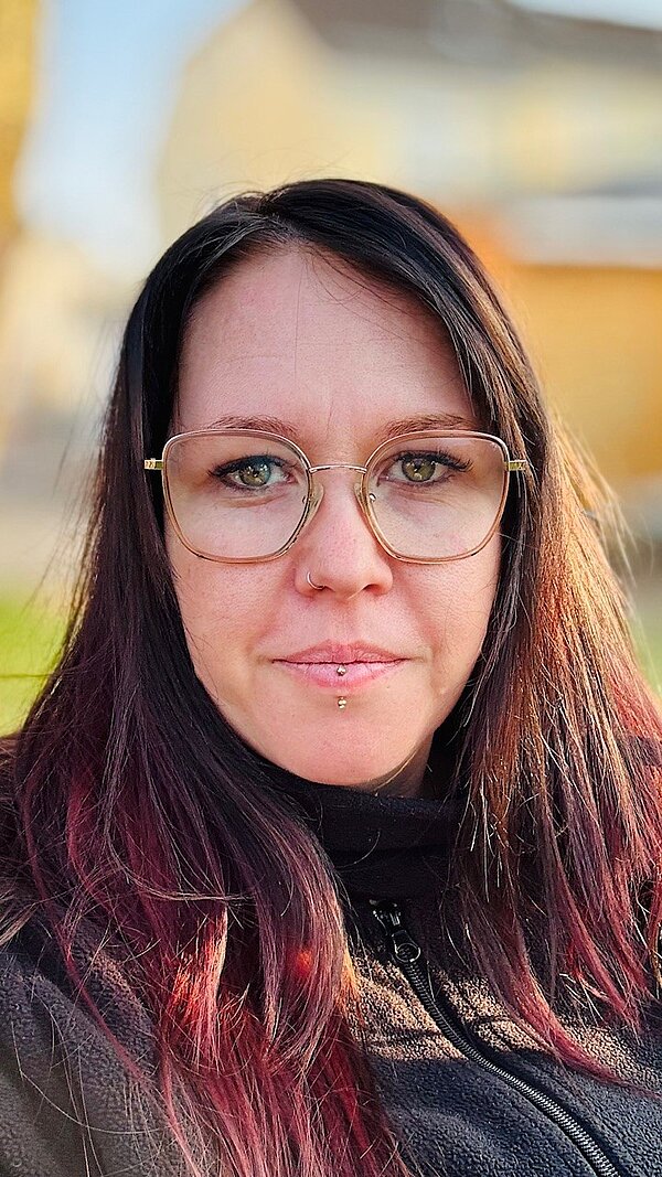 Portrait einer jungen Frau mit Brille und langem braunem Haar.