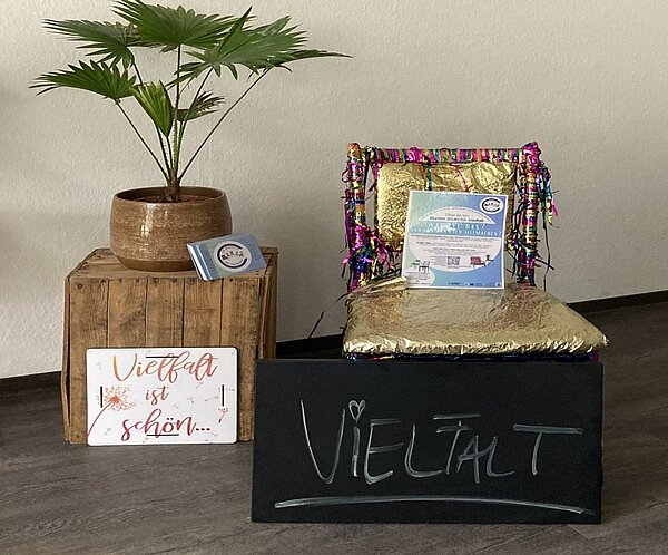 Eine dekorative Theke mit einem Schild 'Vielfalt', einem Blumentopf mit einer Pflanze und einem Stapel Informationsmaterialien.