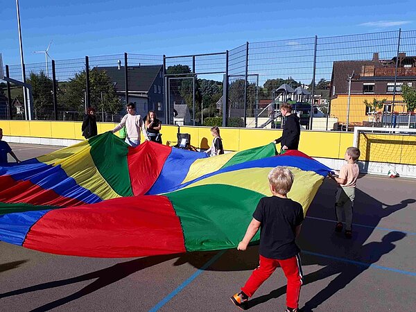 Auszubildende der Sozialassistenz spielen mit den Kindern mit einem bunten Schwungtuch.