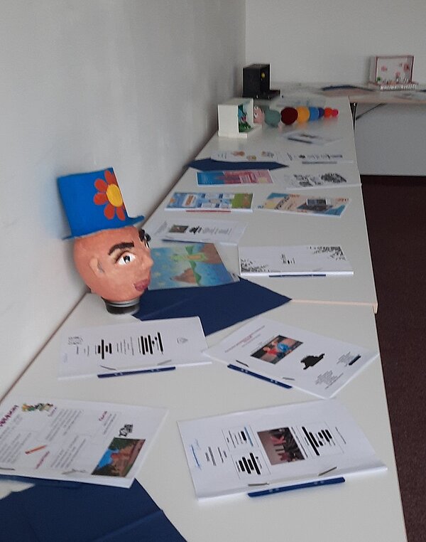 Auf langen, weißen Tischen liegen Informationsmaterialien aus.