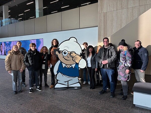 Eine Gruppe Schüler steht um eine Figur des Mainzelmännchens, das sich zwei Finger vor ein Auge hält.