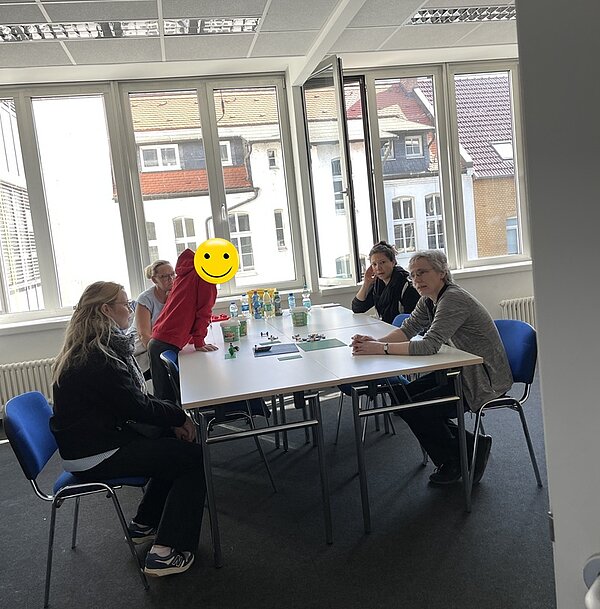 Erfolgreicher Tag der offenen Tür Besucher*innen sitzen gemeinsam an einem großen Tisch, auf dem unter anderem Getränke stehen.