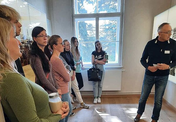 Besuch der Gedenkstätte Großschweidnitz Schülerinnen und Schüler hören aufmerksam einem Museumsführer zu, der vor einem Bildschirm etwas erklärt.