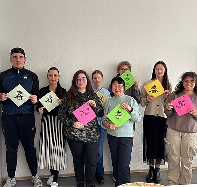 Eine Gruppe von Schülerinnen und Schülern hält bunte Blätter mit ihren Kalligraphien hoch.