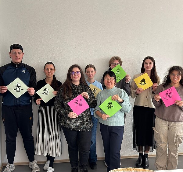 Eine Gruppe von Schülerinnen und Schülern hält bunte Blätter mit ihren Kalligraphien hoch.