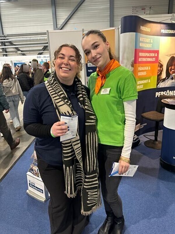 Zwei Frauen stehen lächelnd in einer Messehalle.