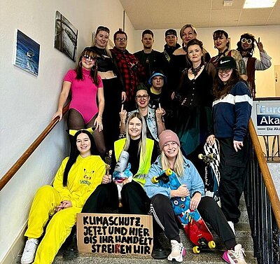 Alle Azubis und Mitarbeitenden posieren auf Treppenstufen in unterschiedlichen Kostümen für ein Gruppenfoto.