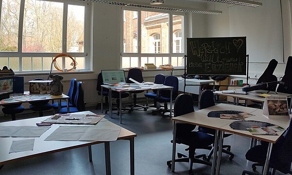 Erfolgreicher Tag der offenen Tür Blick in den Klassenraum, mit Tischen, Stühlen, einem Tafel, auf der die Besucher*innen willkommen geheißen werden.