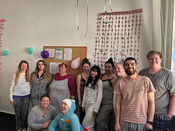 Gruppe von Schüler*innen steht in einem festlich dekorierten Raum mit Luftballons und Partyschmuck.