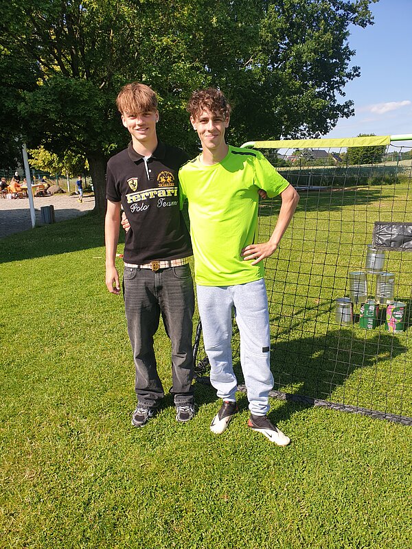 Ein erlebnisreicher Vormittag voller Spiel, Kreativität und Gemeinschaft Zwei junge Männer stehen auf einer Wiese vor einem Fußballtor mit Dosen, die zum Abschießen aufgestellt sind.