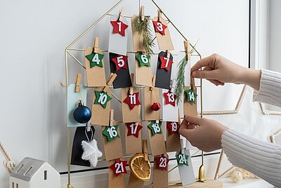 Handgemachter Adventskalender. Wäscheklammern halten die an Drahthaus befestigten Zahlen und Weihnachtsdekoration.