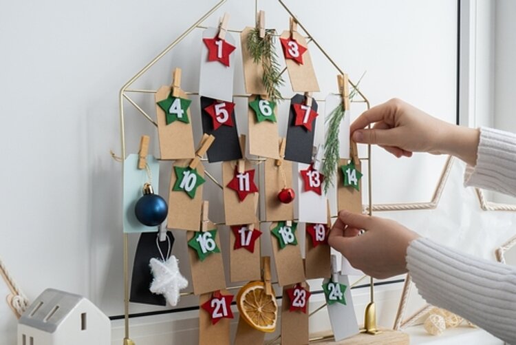Handgemachter Adventskalender. Wäscheklammern halten die an Drahthaus befestigten Zahlen und Weihnachtsdekoration.